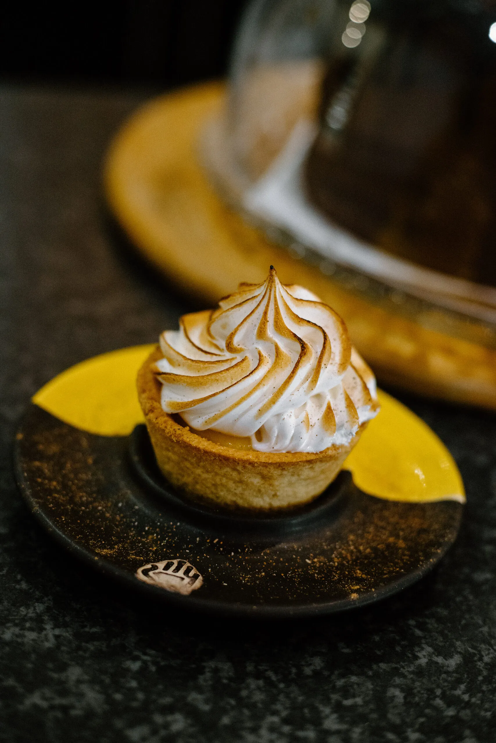 A lemon meringue tartlet on a yellow and black saucer