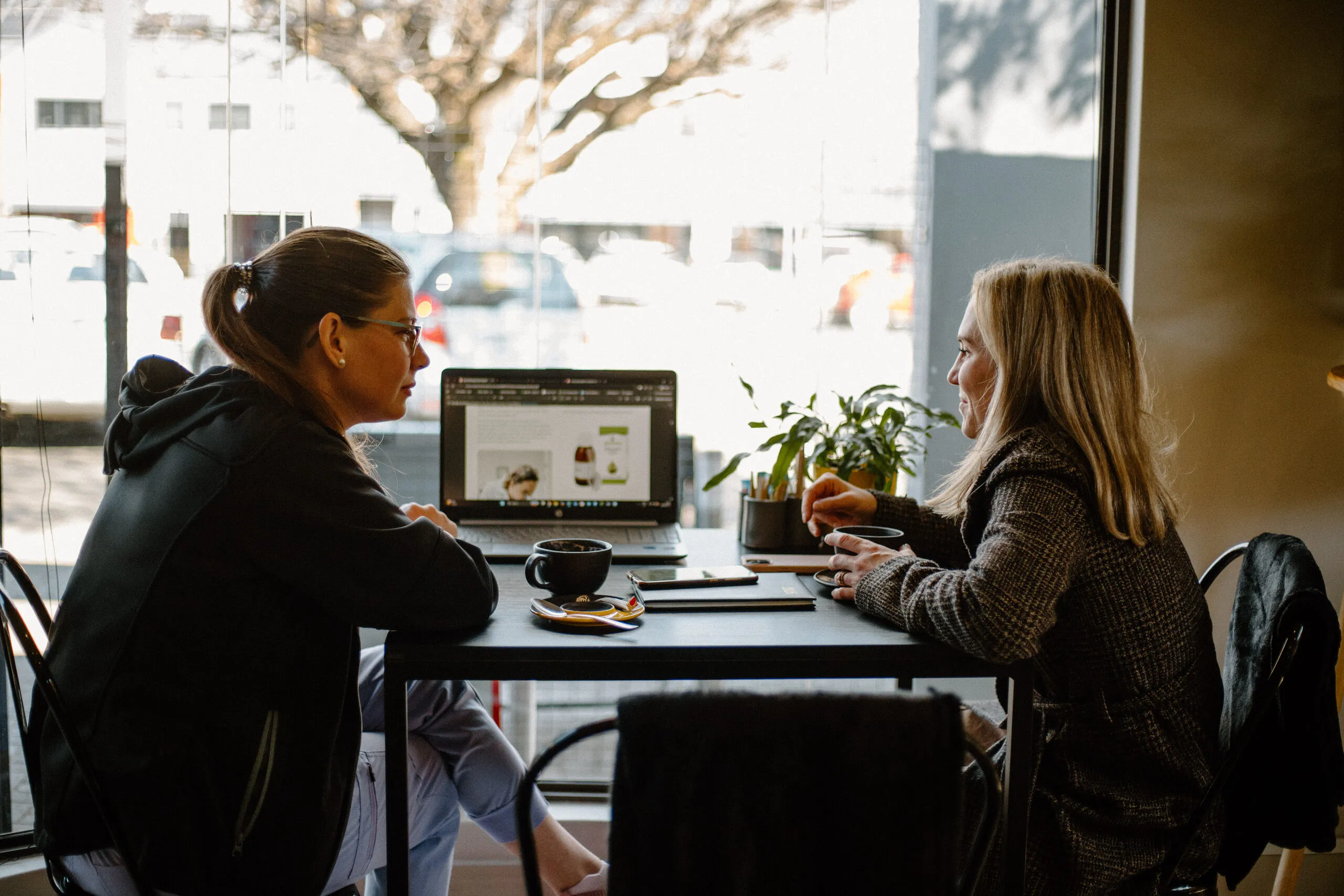 Two customers chatting over coffee at a window table inside Yello Coffee