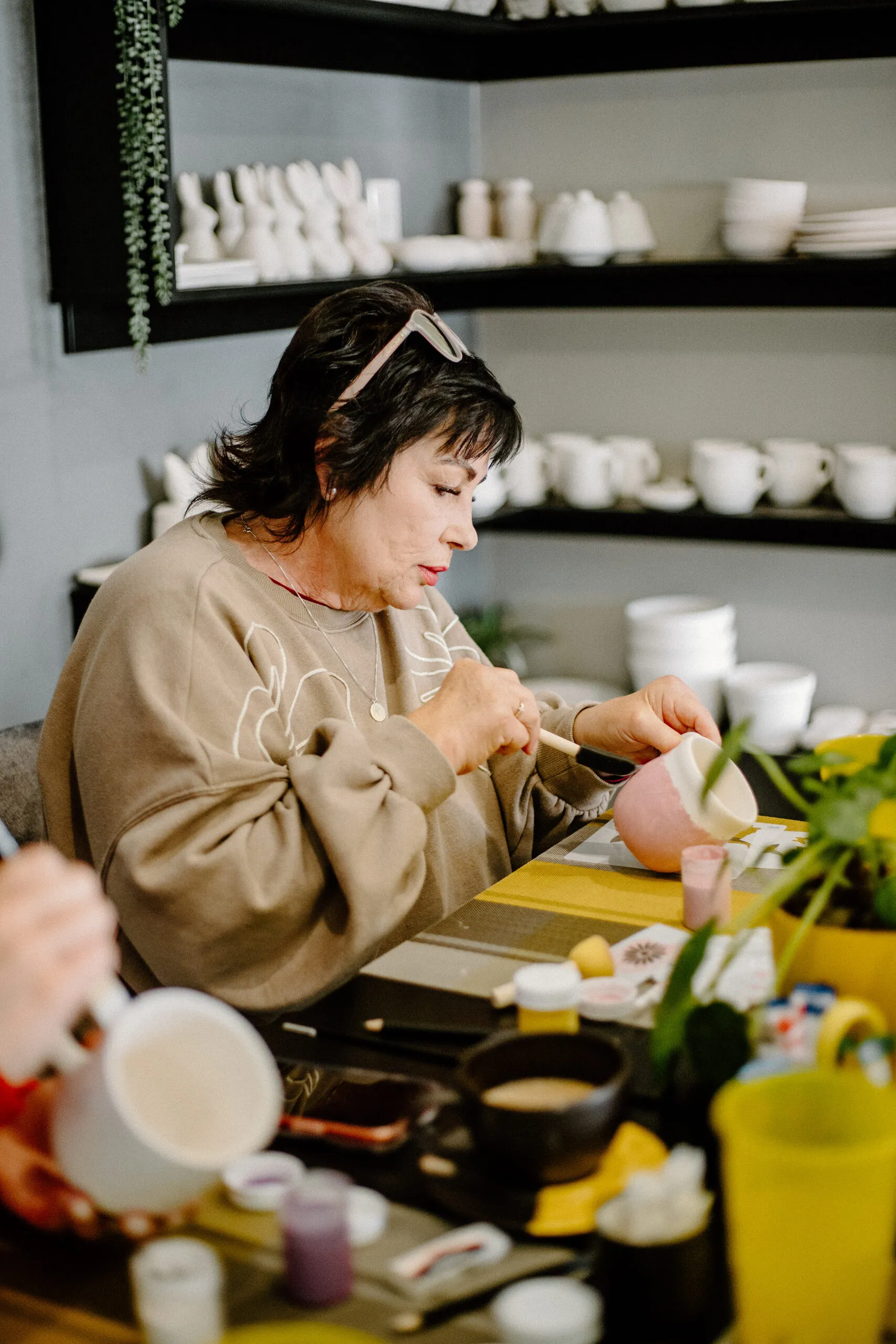 A customer painting pottery at a table with paints and brushes