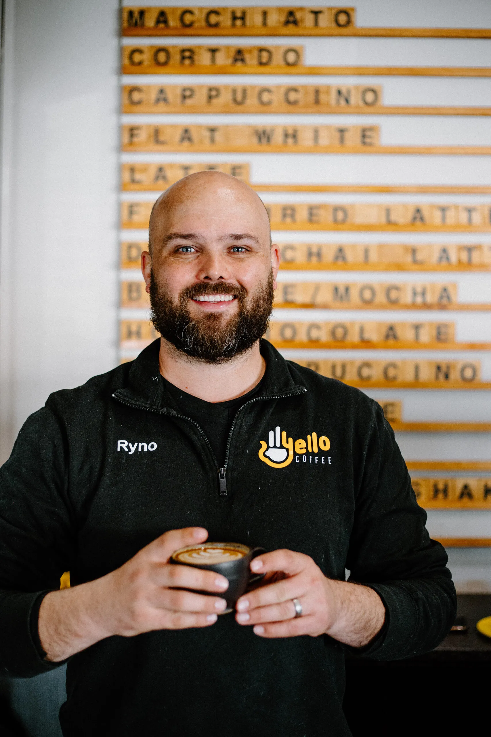 Ryno behind the counter in front of the Yello Coffee menu board